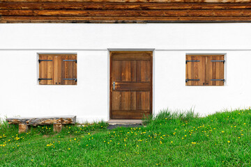Closed wooden door and windows on white wall with green lawn. House exterior concept.