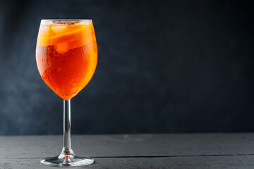 Aperol Spritz cocktail in glass with fresh orange on dark wooden boards. Glass of Aperol Spritz cocktail served in a wine glass. Copy space