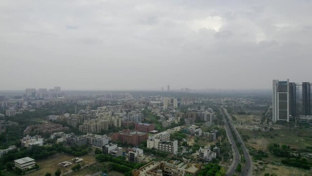 aerial drone shot on a cloudy overcast day showing cityscape of gurgaon with small houses, skyscrapers with homes houses, offies and shopping centers in the city of gurgaon delhi India