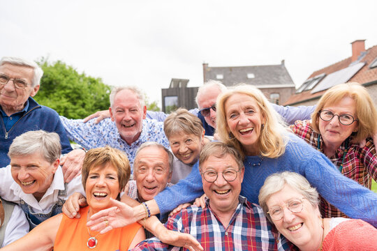 Carefree and happy elderly friends embrace joyfully and taking selfie outdoor in the garden.