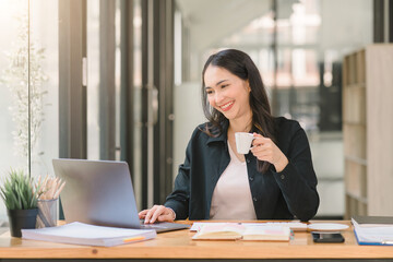 An attractive, young, and confident mixed-race asian businesswoman is sitting at the office table,...