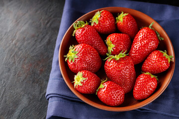 Fresh ripe strawberry in bowl on dark background. Clay bowl with strawberries on blue napkin. Copy space. Top view
