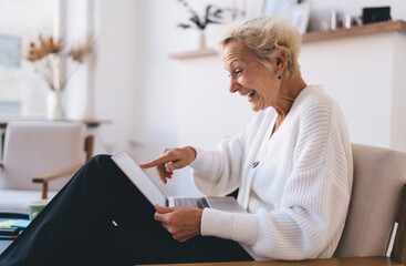 Cheerful mature woman reading book in laptop in living room