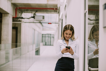 Young business woman using mobile phone in the office hallway