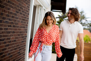 Smiling young couple in love walking in front of house brick wall
