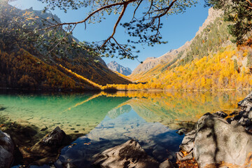 Fototapeta na wymiar Mountain lake with transparent water, sunny weather and autumnal trees.