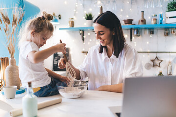 Mother and daughter enjoying preparation of dough at kitchen