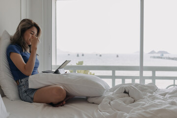 Asian woman works digital online on her bed feeling tired on vacation.
