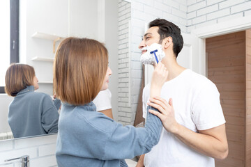 Young attractive woman helps her husband shaving in the bathroom	