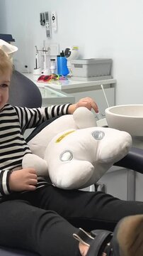 a little girl in a striped blouse in a dental office with a soft toy A sleepwalker or white astronaut laughs hugging waiting 