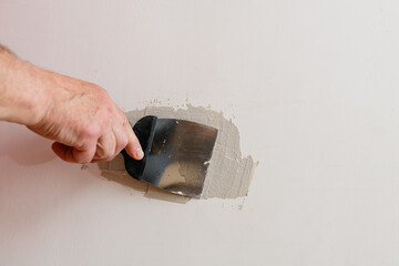 Repairing holes in drywall. A handyman is repairing a hole in the drywall in the wall. - 616513422