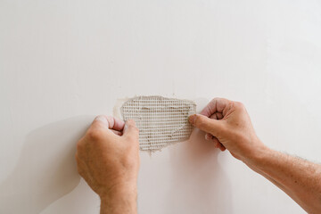A handyman is repairing a hole in the drywall in the wall. - 616513427