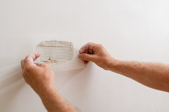 A handyman is repairing a hole in the drywall in the wall.