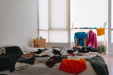 Cluttered and untidy apartment bed room full of colorful clothes on everywhere.