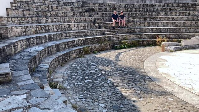 A couple of tourists sit on the stone steps of the ancient odeon where Roman leaders would hold council - Plovdiv, Bulgaria, Europe