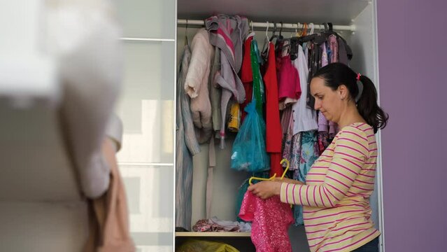 Young woman tidying up clothes in wardrobe, hanging clothes on hangers. Housewife general cleaning at home