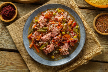 Israeli style couscous with sumac and pieces of stewed chicken on a table on a linen napkin in a plate next to spices