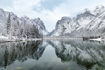 Beautiful view of Dobbiaco Lake (Toblacher See) on a snowy winter day, with reflections of mountains in the Dolomites, Bolzano, Italy
