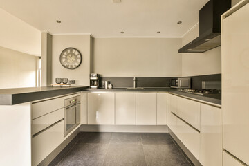 a kitchen with black counter tops and white cupboards on the wall behind it is a large clock in the...