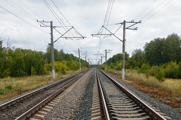 Fototapeta na wymiar Two long and straight lines of railway rails with electric poles inside,