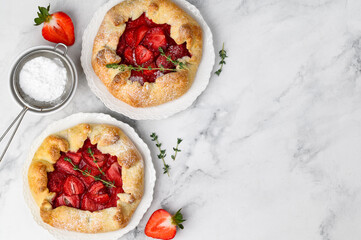 Two strawberry galettes decorated with thyme and powdered sugar on plates on a marble background. Copy space, top view