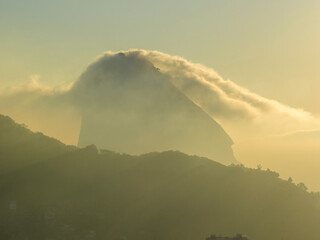 Aerial view of Sugarloaf Mountain wrapped in clouds at dawn under the sun's rays. Rio de Janeiro....