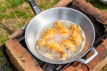 chicken drumstick in batter is fried in oil in a wok in the country. Cooking delicious food at a picnic