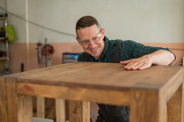 Male carpenter finishing work on wooden table in workshop. 