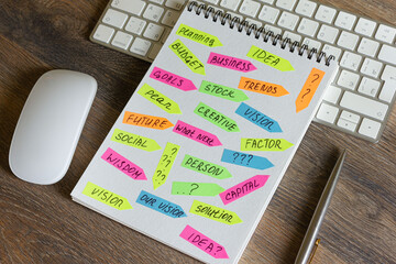 On a wooden table is a keyboard and mouse, a pen with a notepad with stickers with inscriptions on it.