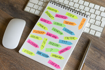 On a wooden table is a keyboard and mouse, a pen with a notepad with stickers with inscriptions on it.