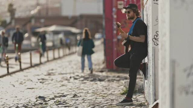 A man standing by the wall and playing guitar on the street