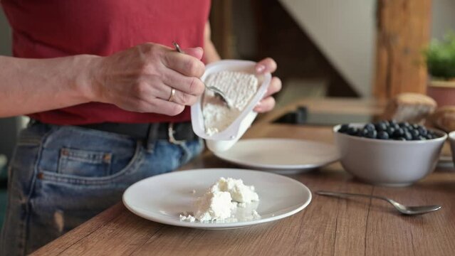 Girl hands put cottage chease at plate for healthy breakfast at home. Young woman preparing milk cream desert for organic meal nutrition