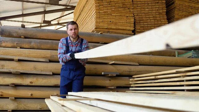 Worker unload and rearrange wooden boards on a summer day outdoors. Storage of lumber for construction in an open warehouse