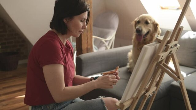 Pretty girl artist drawing sketch with golden retriever dog using pencil and canvas. Beautiful young woman painting portrait of cute doggy pet
