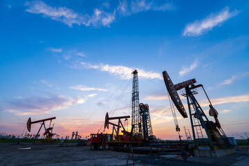 in the evening, oil pumps are running, The oil pump and the beautiful sunset reflected in the water, the silhouette of the beam pumping unit in the evening.