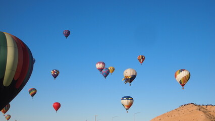 Multiple hot air balloons in flight across the blue sky