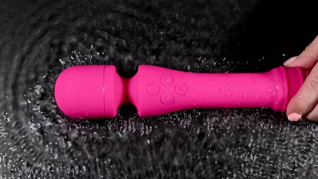 A woman is holding a pink vibrator in water. Sex toy on a black background.