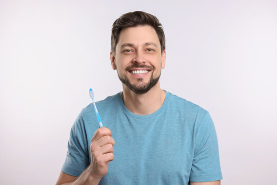 Happy man holding plastic toothbrush on white background. Mouth hygiene