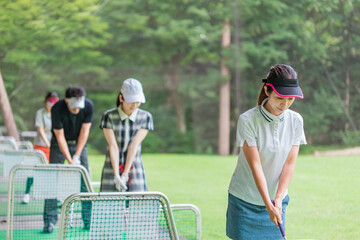 ゴルフ練習場・打ちっぱなし・ゴルフセンターでスイングの練習するゴルフ選手・ゴルファーの男女
