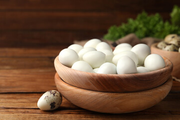 Fototapeta na wymiar Many peeled boiled quail eggs and another one in shell on wooden table, closeup