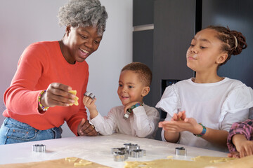 Happy african mother and children cutting cookie shapes in a cookie dough in the kitchen.