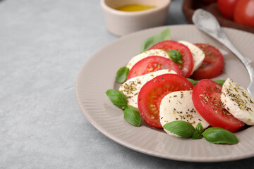 Delicious Caprese salad with tomatoes, mozzarella, basil and spices on light grey table, closeup
