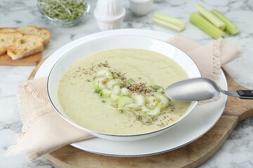 Bowl of delicious celery soup and spoon on white table, closeup