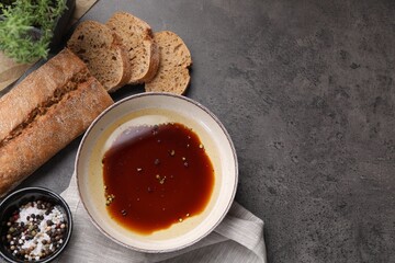 Bowl of balsamic vinegar with oil, spices and bread on dark grey table, flat lay. Space for text