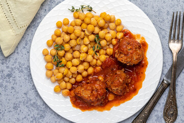 meatballs coated in a red tomato-based sauce, accompanied by chickpeas and garnished with fresh herbs