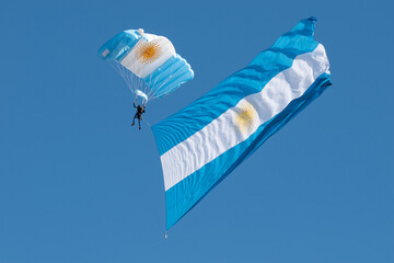 paratrooper with his parachute deployed in Argentine colors holds a large fluttering Argentine flag