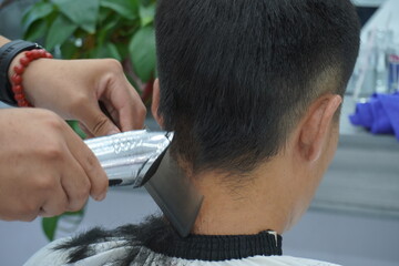 hairdresser makes a haircut for Asian man with a scissors in a barbershop. professional services. beauty salon for men. cosmetics and products for scalp and hair care. close up.