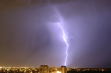 Massive cloud to ground lightning bolts hitting the horizon of city lights