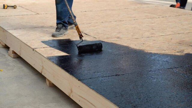 Applying hot resin to the floor for waterproofing, roller and bucket of resin, black and liquid resin