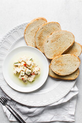 Top view of marinated feta cheese cubes and slices of toasted bread on a white plate. Cheese cubes in a ramekin with bread, flat lay of feta cheese cubes and slices of toast